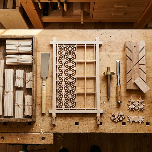 Top-down flat-lay of woodworker bench during kumiko assembly with tools and basswood strips